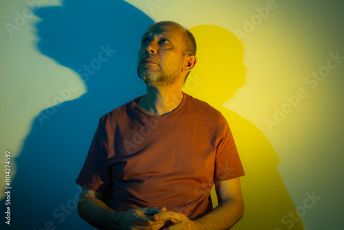 White man leaning against a wall with blue and yellow colored lights above him. Studio portrait.