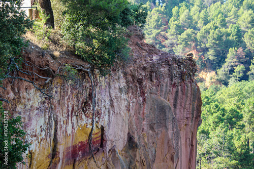 Ockerfelsen in den Farben Rot, Ocker, Gelb und Orange vor Wald und Bergen in Roussillon, Frankreich