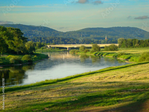 Flusslauf führt durch gemähte Wiesen auf eine Brücke zu