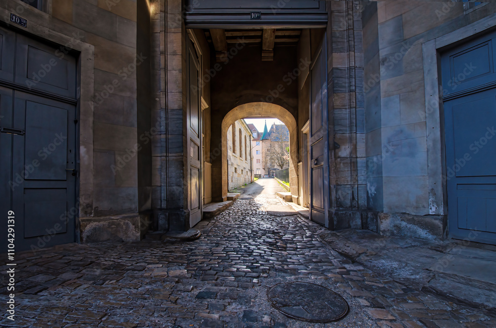 An old street with an arch in the old part of Besancon. France. There are beautiful stone walls and pavement. A small fortress tower is visible in the distance. An old street with an arch in the old part of Besancon. France. There are beautiful stone walls and pavement. A small fortress tower is visible in the distance.