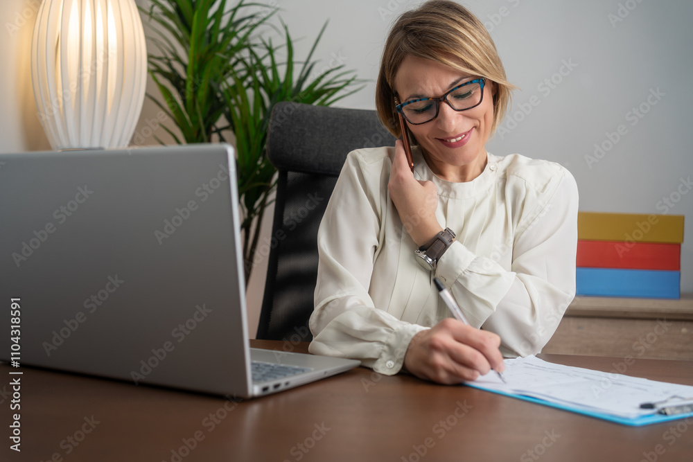 Cheerful mature businesswoman sitting at her workplace. Happy mature businesswoman working at her desk in the office. Smiling mature businesswoman focused on her tasks at work.
Cheerful mature businesswoman sitting at her workplace. Happy mature businesswoman working at her desk in the office. Smiling mature businesswoman focused on her tasks at work.