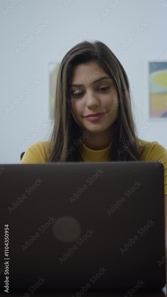 Dolly out of confident and cheerful caucasian brunette woman opening and typing on a laptop. Young female professional writing an important email from her home. Modern living room. Remote working.