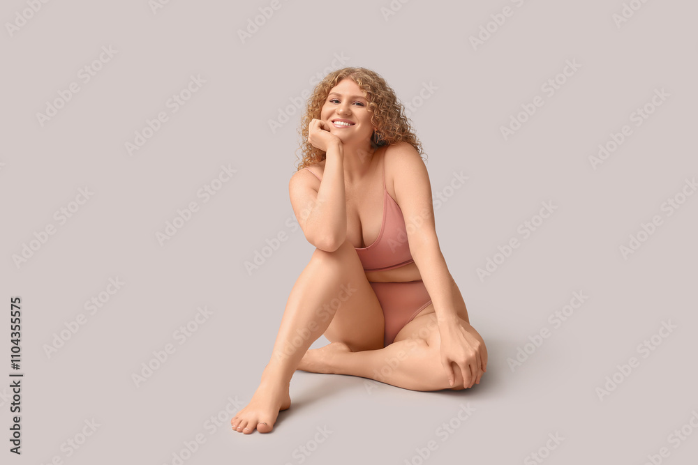 Beautiful young happy body positive woman in trendy underwear sitting on grey background Beautiful young happy body positive woman in trendy underwear sitting on grey background
