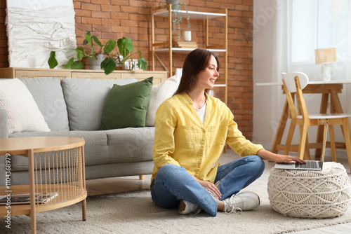 Young woman using laptop on pouf at home