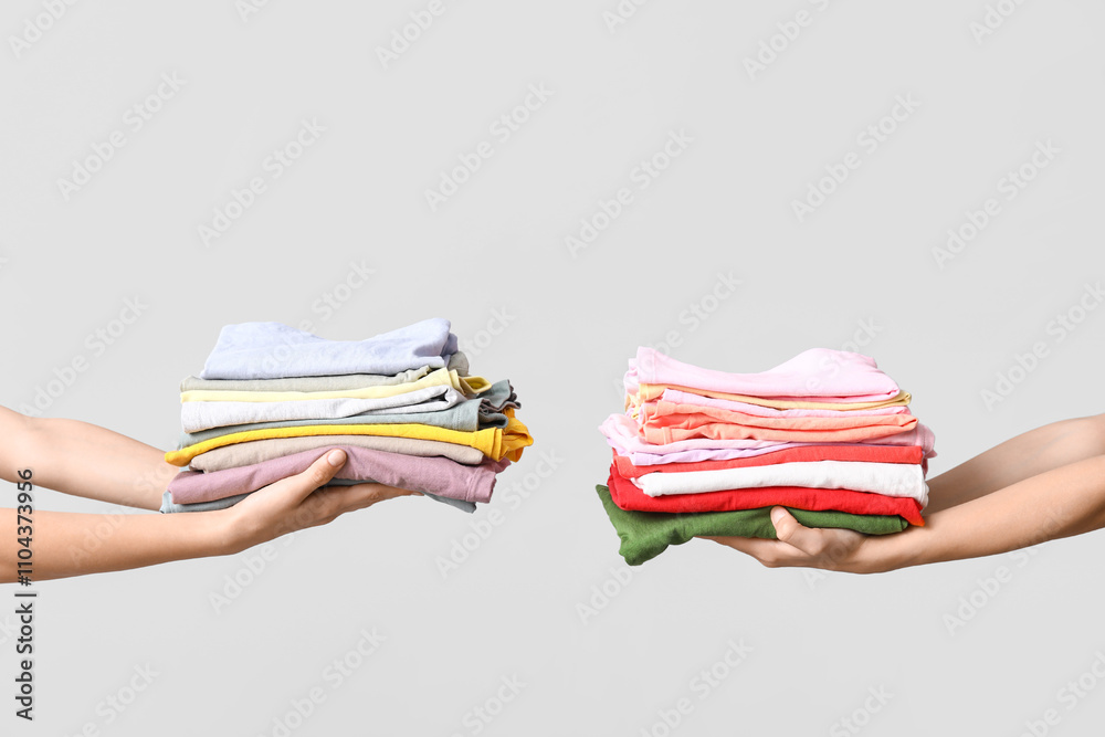 Female hands with stacks of different clothes on grey background Female hands with stacks of different clothes on grey background