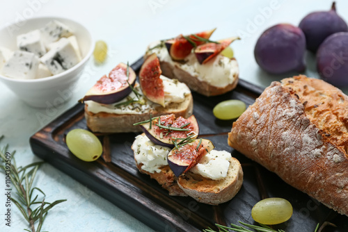 Wooden board of delicious fig bruschetta with rosemary and bowl of blue cheese on light blue background, closeup photo