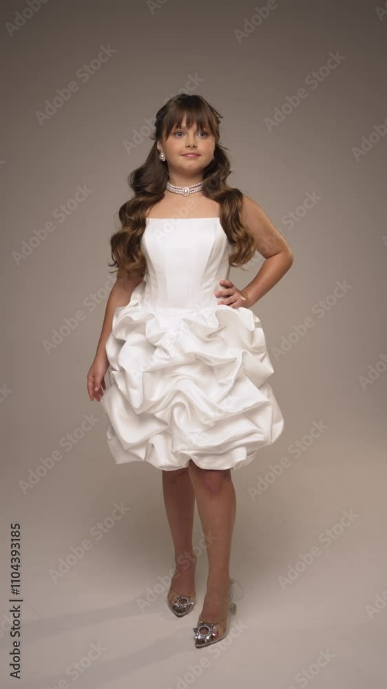 Teenage girl in elegant white dress poses in studio. Concept of posing in photo studio. Teenage girl in elegant white dress poses in studio. Concept of posing in photo studio.