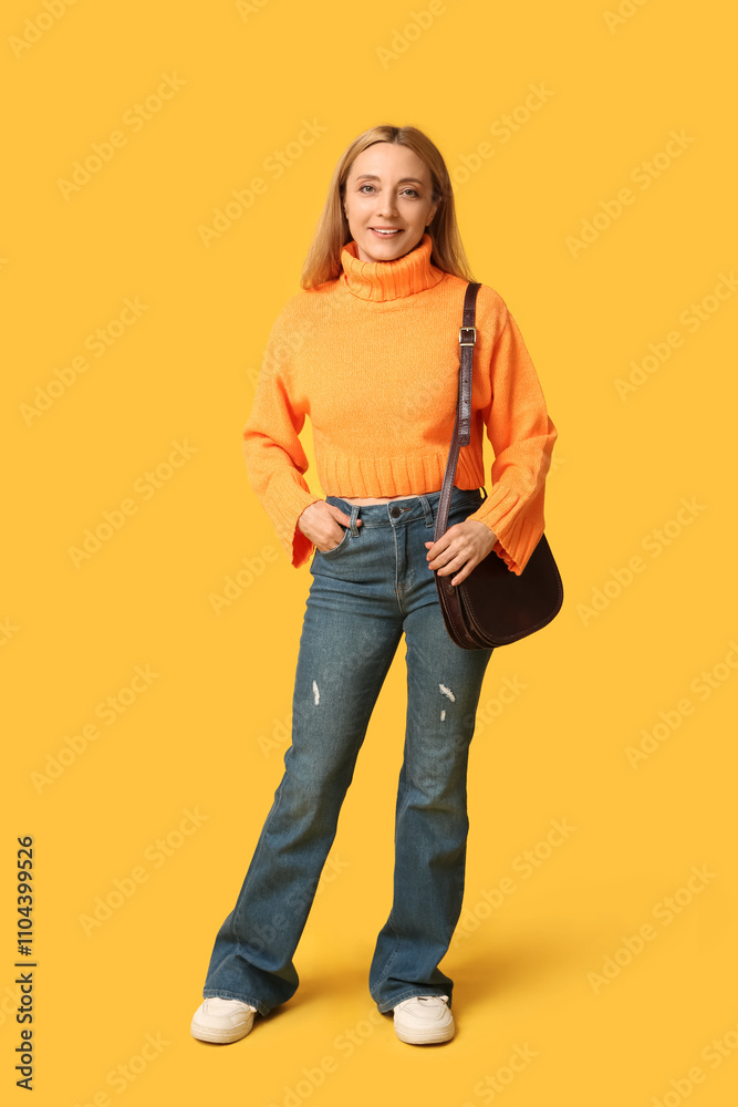 Beautiful mature woman in stylish orange sweater with brown bag on yellow background Beautiful mature woman in stylish orange sweater with brown bag on yellow background