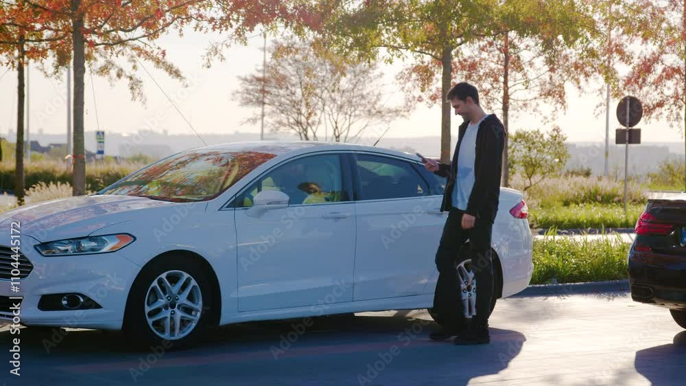 Man with telephone goes towards ordered car-sharing vehicle