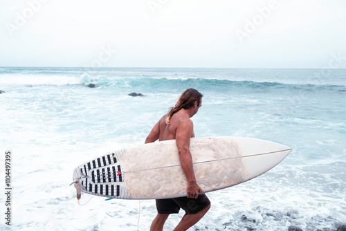 senior man entering the sea to surf with a surfboard.