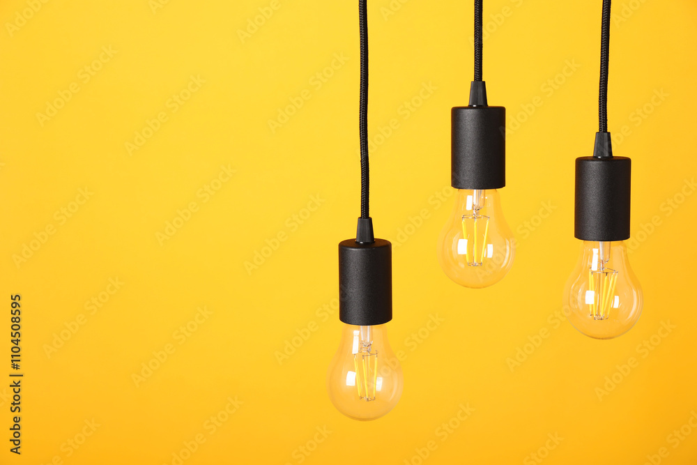 Light bulbs hanging on cords against orange background, space for text Light bulbs hanging on cords against orange background, space for text