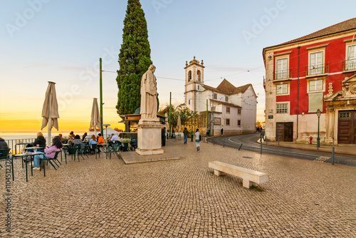 Sunset view from a sidewalk cafe near the Beco de Santa Helena observation viewpoint, of the Sao Vicente statue and Igreja de Santa Luzia church tower in Lisbon, Portugal.