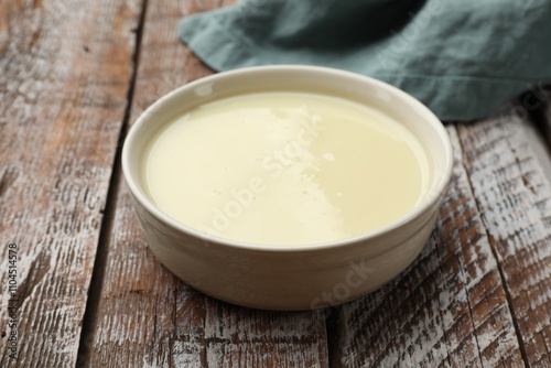 Condensed milk in bowl on wooden table, closeup