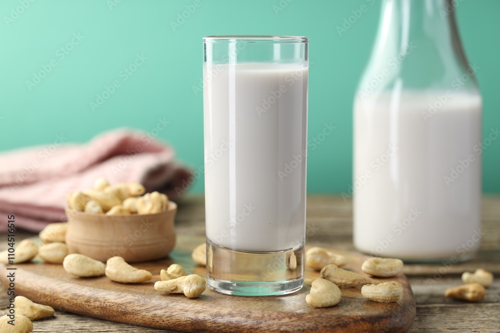 Fresh cashew milk in glass, bottle and nuts on wooden table against green background, closeup Fresh cashew milk in glass, bottle and nuts on wooden table against green background, closeup