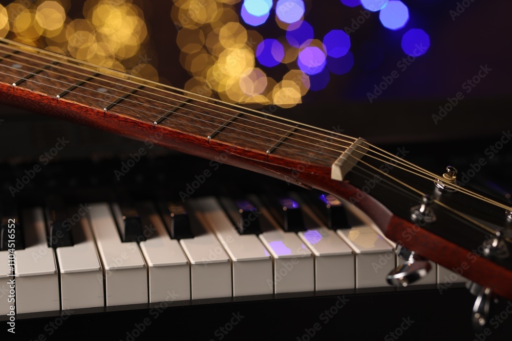 Fototapeta premium Guitar on piano against blurred lights, closeup. Bokeh effect