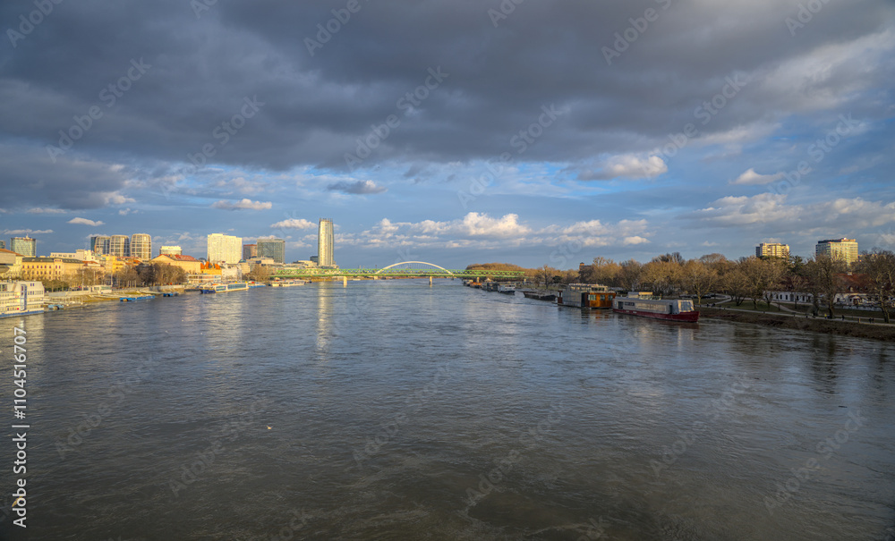 Fototapeta premium Wide view of a river surrounded by a modern cityscape and cloudy skies.