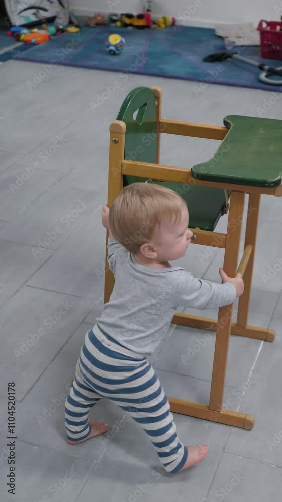 Vertical video of curious toddler enthusiastically moves bright green high chair in cozy home environment, which emphasizes the child's early development and joyful interaction Vertical video of curious toddler enthusiastically moves bright green high chair in cozy home environment, which emphasizes the child's early development and joyful interaction