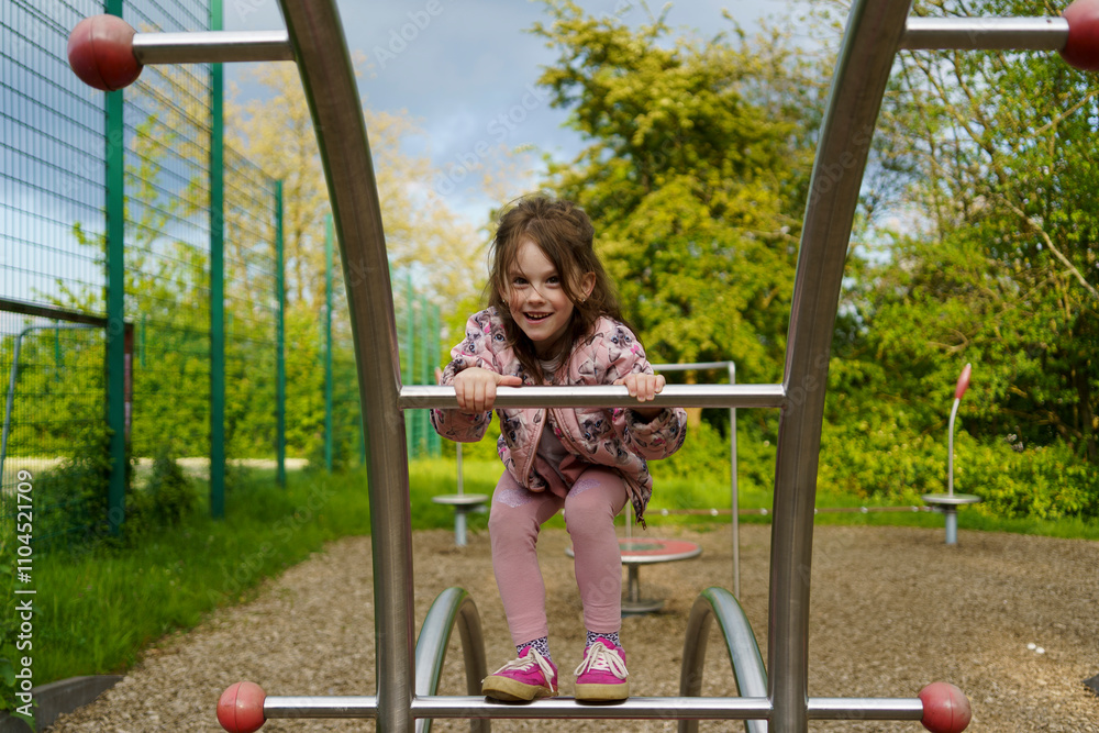 Obraz premium Little girl with long hair climbing on playground in summer. Healthy active mischievous child concept