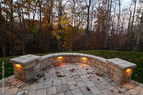 A cozy stone patio illuminated by warm lights during twilight, surrounded by an autumn forest and scattered leaves, creating a serene and inviting evening atmosphere.