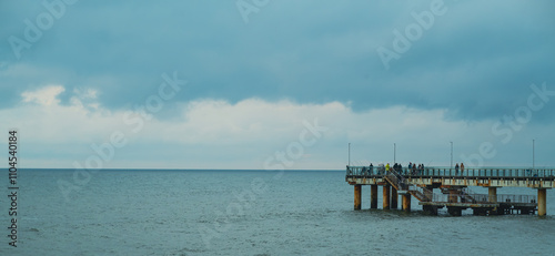 People Walking on a Pier Overlooking the Ocean at Dusk With Dramatic Clouds Above