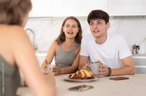 Young girl and guy have nice conversation with woman, mom, during Sunday tea party. Long-awaited family meeting, tea party, casual conversation of relatives in cozy home atmosphere