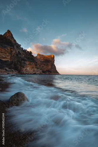 The rock rises above the blue sea at sunset or sunrise