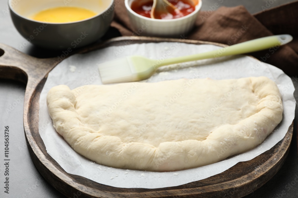 Uncooked calzone pizza, sauce and egg yolk on grey table, closeup Uncooked calzone pizza, sauce and egg yolk on grey table, closeup
