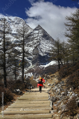 A young woman hiker with backpack walking on hiking trail towards to the mountain. Yading Nature Reserve, Sichuan, China.