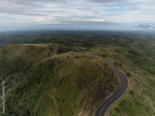  Aerial view of a curvy mountain black top road with beautiful landscape around it.