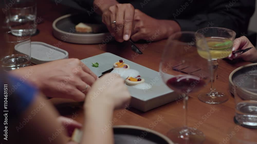 Close-up view of a group of faceless people having dinner together, eating rabbit pate with carrot gel with knife and fork