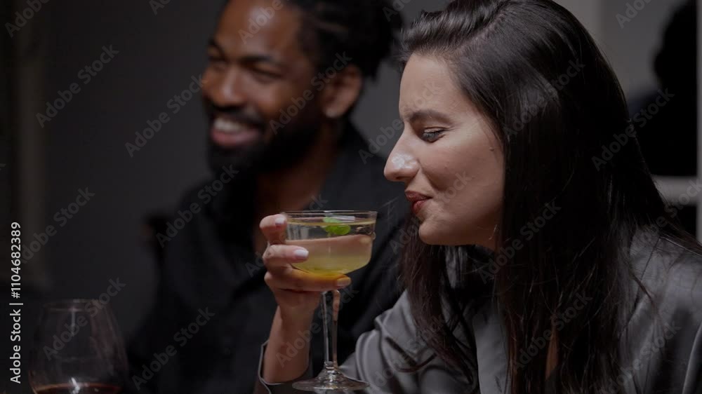 Handheld shot of a young couple sitting at table in restaurant, woman is drinking cocktail while talking and smiling with her boyfriend Handheld shot of a young couple sitting at table in restaurant, woman is drinking cocktail while talking and smiling with her boyfriend