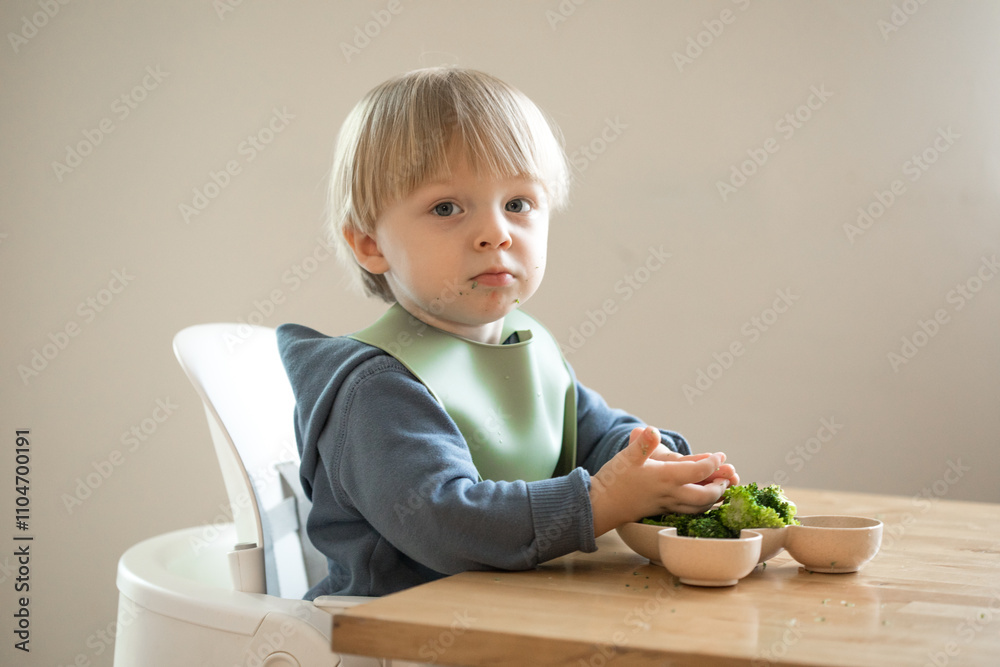 Beautiful baby eating broccoli pieces in his chair Beautiful baby eating broccoli pieces in his chair