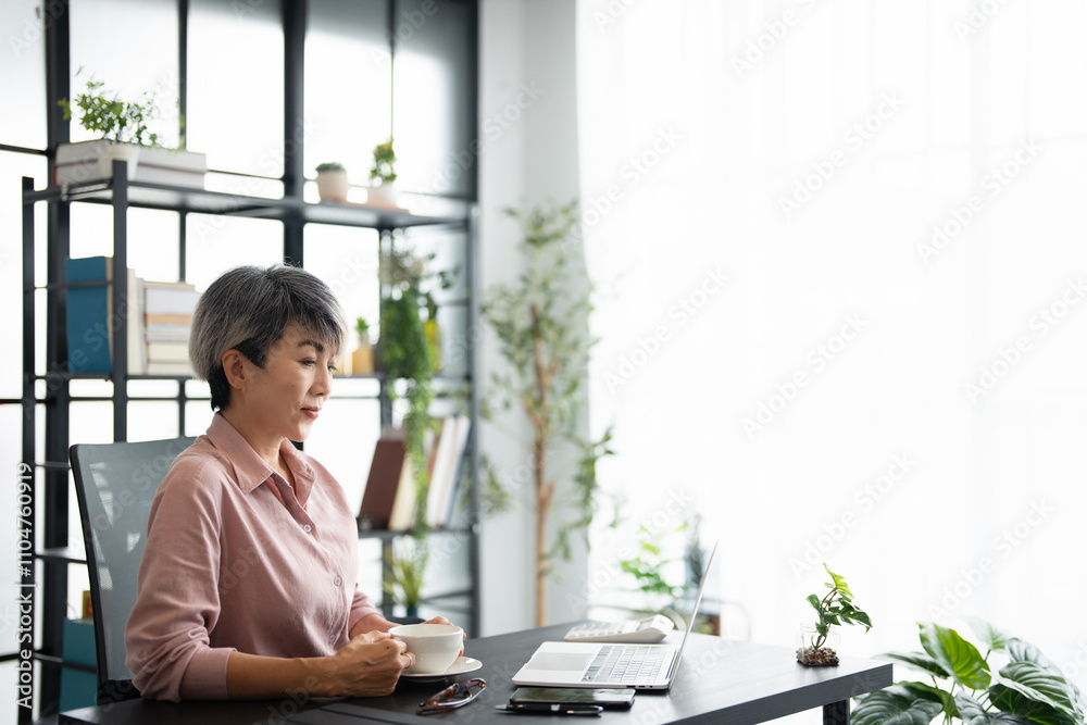 Mature asian business woman drinking coffee and thinking about the strategy of new startup while looking out the window in modern office. copy space Mature asian business woman drinking coffee and thinking about the strategy of new startup while looking out the window in modern office. copy space