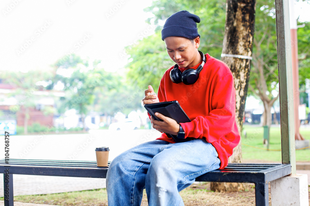 Obraz premium Cheerful Young Freelancer Guy Working Using Digital Tablet While Sitting on Bench