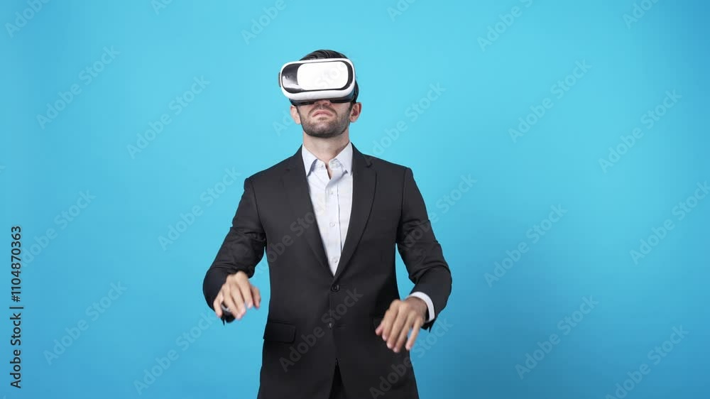 Businessman moving hand and managing data by using augmented reality technology. Caucasian investor wearing VR glasses and planning marketing strategy while standing at blue background. Apparatus. Businessman moving hand and managing data by using augmented reality technology. Caucasian investor wearing VR glasses and planning marketing strategy while standing at blue background. Apparatus.