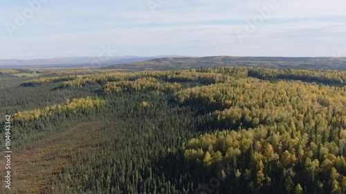 Fall colors blanket the Alaskan wilderness with sunny and cloudy skies and a rural highway cutting through photo