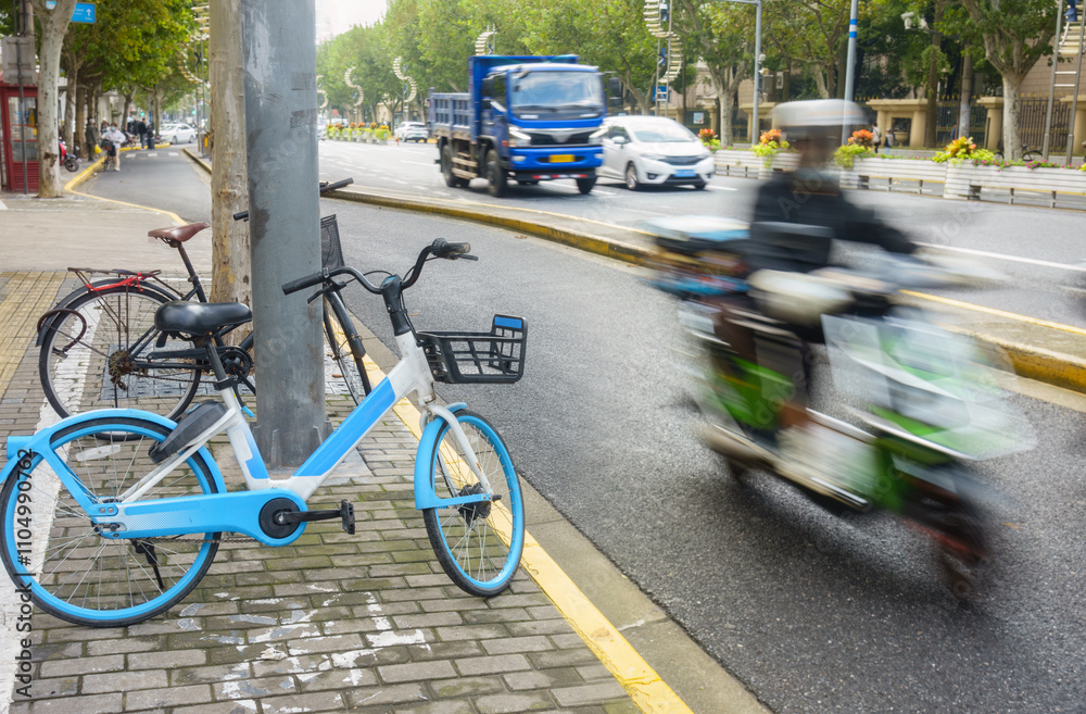 Bicycles parked on the side of the street. Unrecognizable motorists and cars driving on the road. Shanghai.