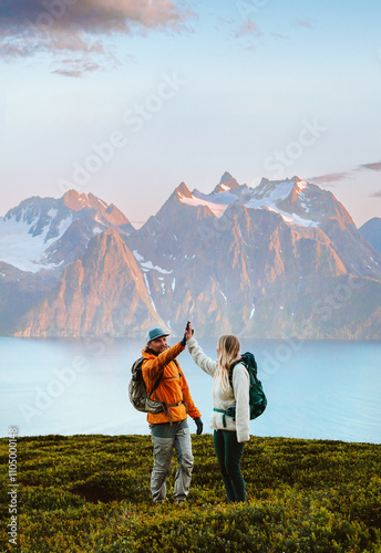Couple man and woman traveling together hiking in Norway, friends high five hands in mountains active vacations healthy lifestyle outdoor family adventure extreme climbing tour, collaboration concept