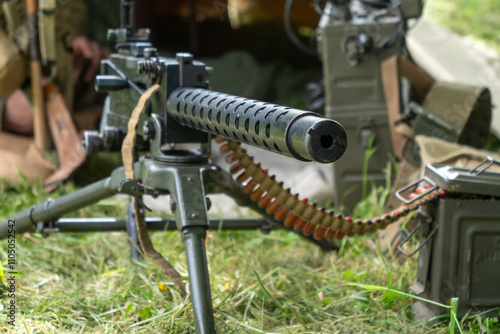 Black machine gun with a long barrel is on a grassy field. The gun is surrounded by a lot of ammunition photo