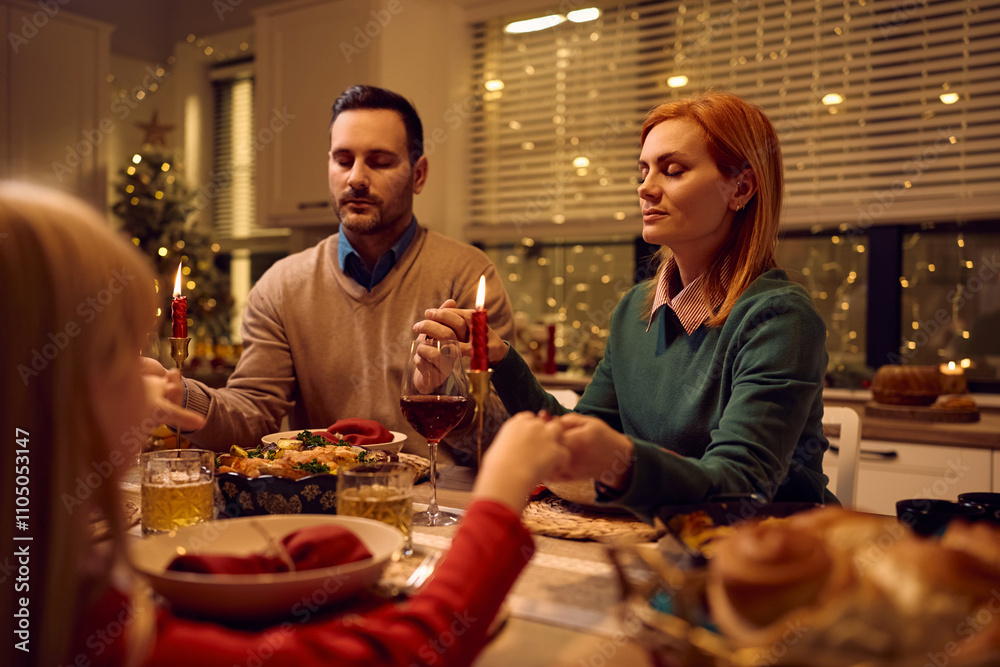 Mid adult woman praying with her family during Christmas meal at dining table. Mid adult woman praying with her family during Christmas meal at dining table.