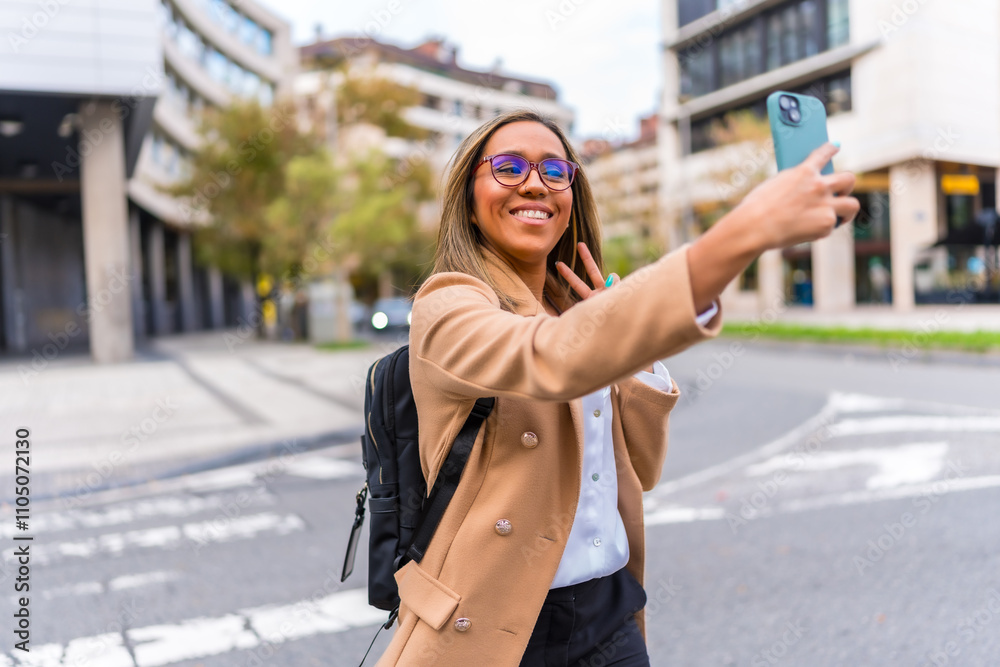 Fototapeta premium Happy latin businesswoman taking selfie standing in the city