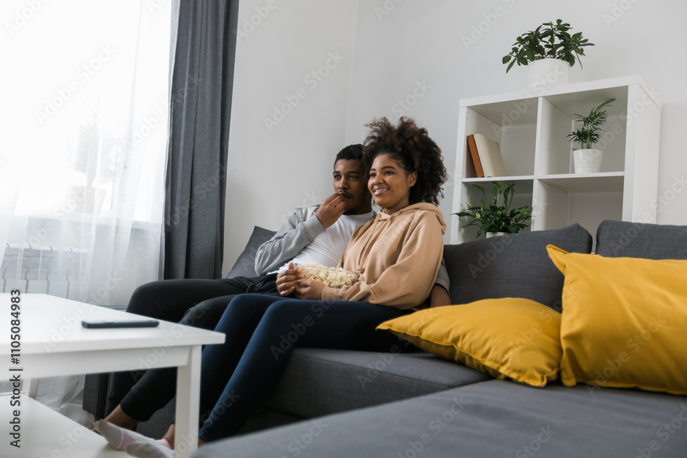 African American couple wife husband watching movie. Family pastime and leisure, watch television, rest. Relaxed man and woman watching TV series together sitting on couch at home enjoying eating African American couple wife husband watching movie. Family pastime and leisure, watch television, rest. Relaxed man and woman watching TV series together sitting on couch at home enjoying eating