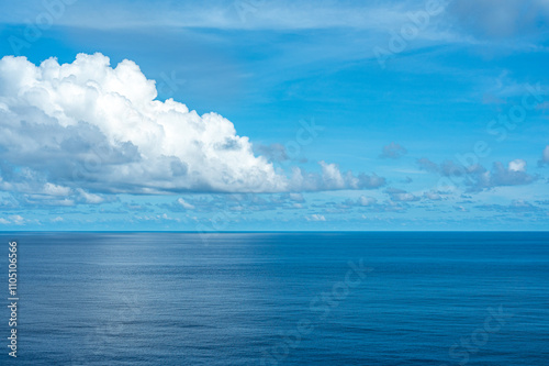 Serene ocean view with clear blue sky and large white clouds, calm water surface reflecting sunlight, peaceful seascape horizon, tranquil nature scene, beautiful weather, scenic coastal landscape