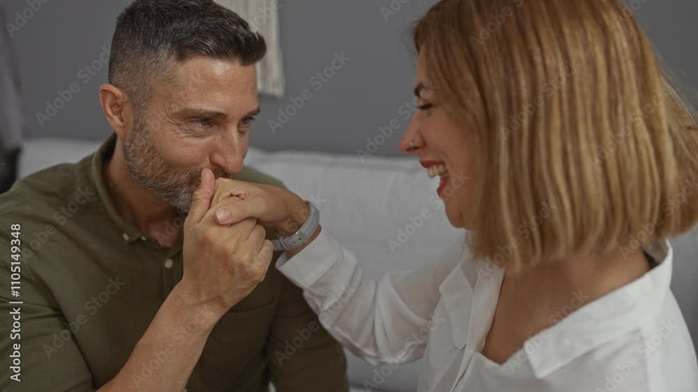 Man kissing woman hand while sitting together smiling lovingly in the cozy setting of their home living room Man kissing woman hand while sitting together smiling lovingly in the cozy setting of their home living room