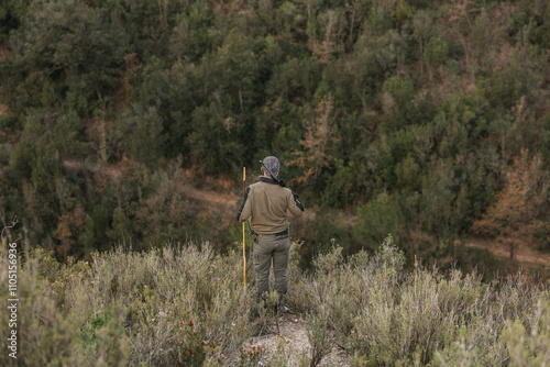 Hunter standing on hill looking at forest with rifle photo