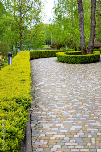 Obraz na płótnie Curved stone pathway lined with vibrant green hedges in a serene garden setting w salonie