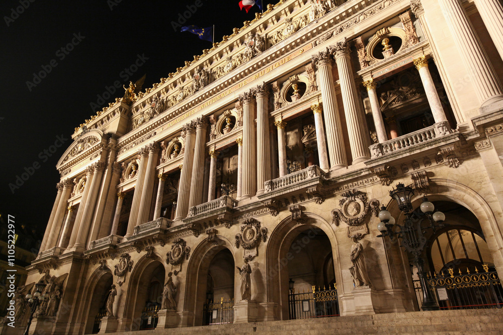 Obraz premium The iconic facade of the Palais Garnier Opera House in Paris, illuminated at night, showcasing its ornate architecture with golden statues and intricate details under a clear sky