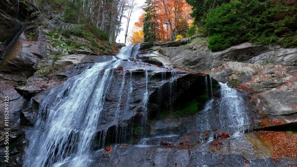 Silky waterfall flowing through an autumn forest, surrounded by fallen leaves and tranquil scenery, creating a harmonious natural landscape. Aerial nature video.