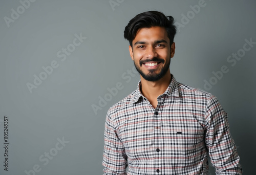 Young man with beard smiles warmly in plaid shirt.