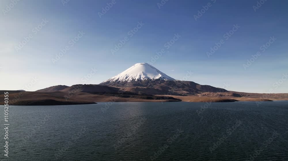 Aerial View Of Vulcan Parinacota In Lauca National Park, Chile, Captured On A Sunny Autumn Day. The Drone Ascends From The Lake, Revealing Snow-Capped Peaks And Sandy Terrain Below. Aerial View Of Vulcan Parinacota In Lauca National Park, Chile, Captured On A Sunny Autumn Day. The Drone Ascends From The Lake, Revealing Snow-Capped Peaks And Sandy Terrain Below.
